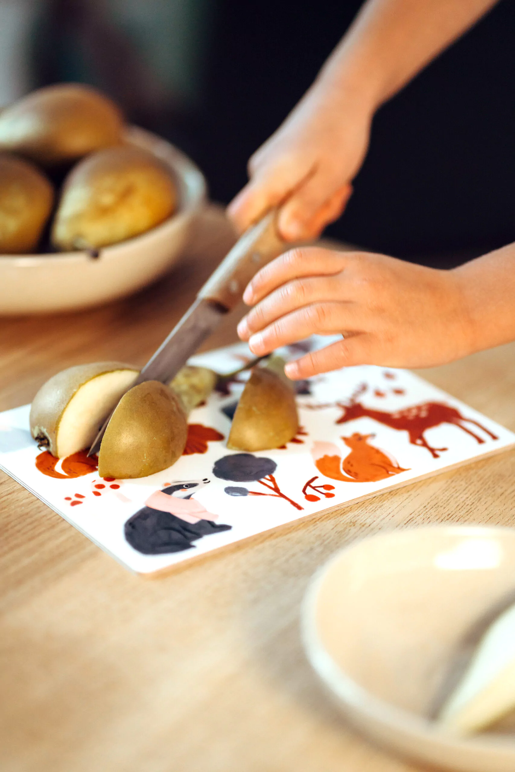 nuukk, Tisch mit Schneidebrett / Frühstücksbrettchen für Kinder, Motiv: Waldtiere. Kind schneidet Birne